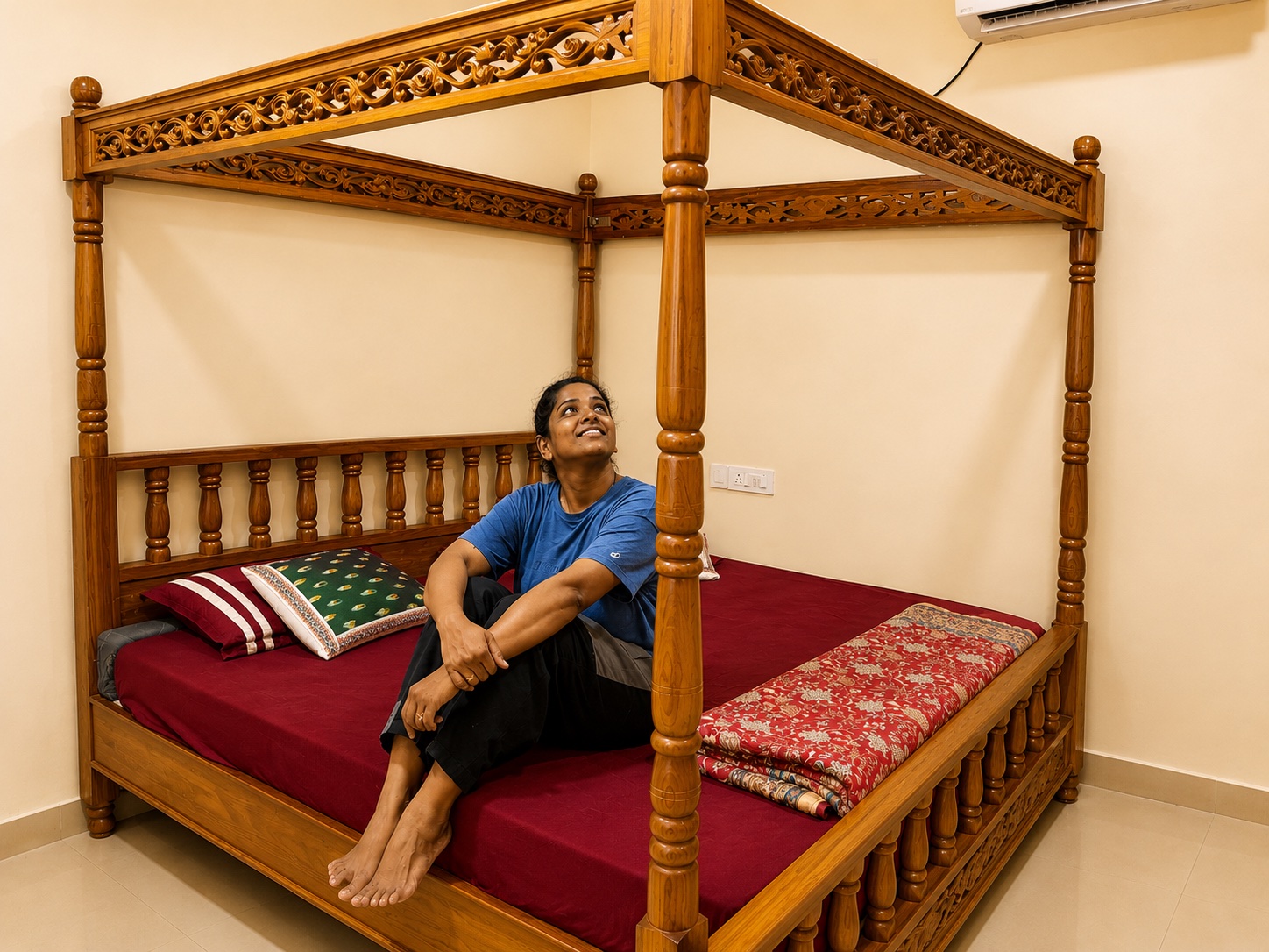 The same four-poster bed, with someone sitting on it looking up at the carved canopy