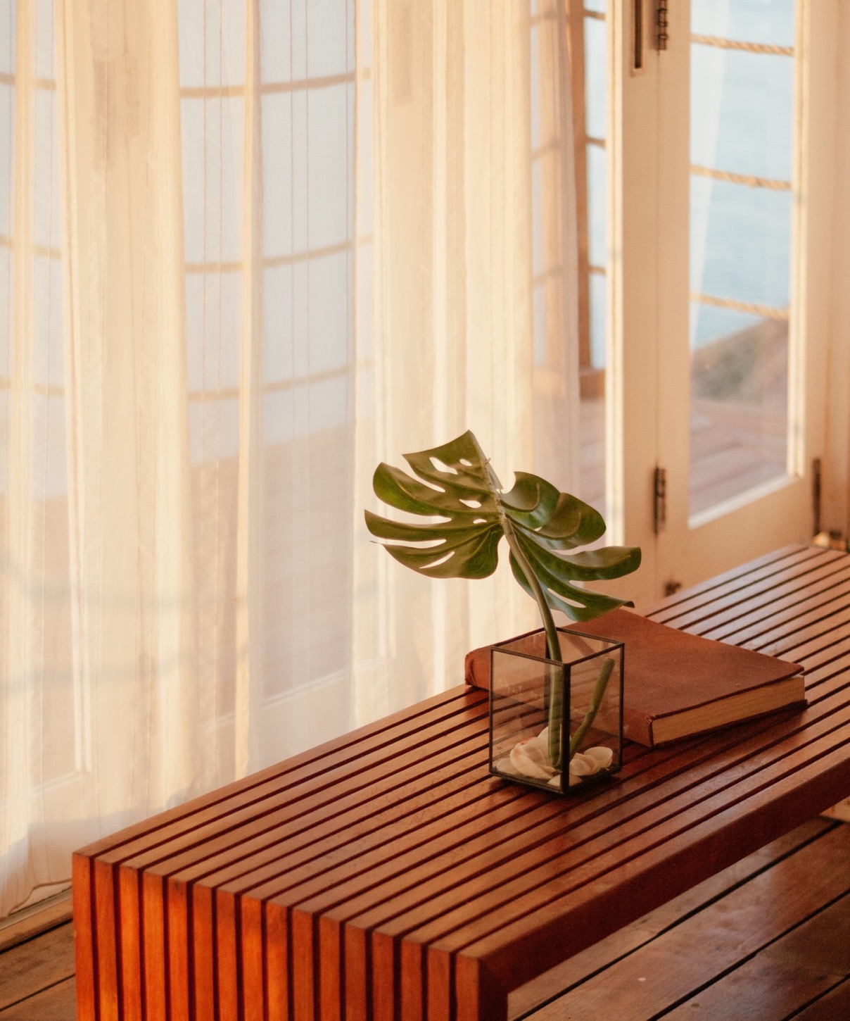A slatted timber bench in warm light beside a curtained window