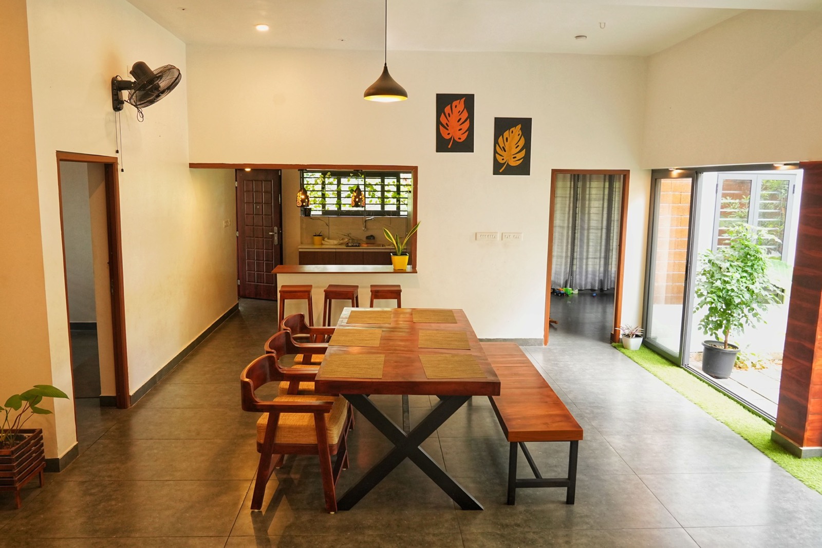 A dining table with a timber slab top and cane-backed chairs in a modern room open to a courtyard